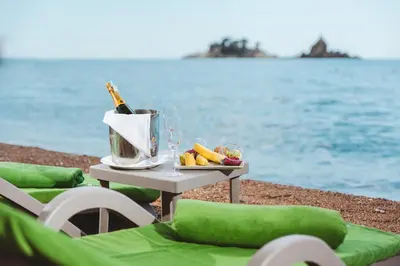a table with a bottle of wine and fruit on the beach at Hotel AMI Budva Petrovac in Petrovac na Moru