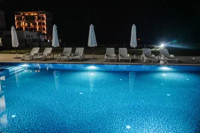 a swimming pool with chairs and umbrellas at night at La Dolce Vita Residence in Ulcinj