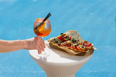 a person holding a drink next to a plate of food at Hotel Harmonia by Dukley in Budva