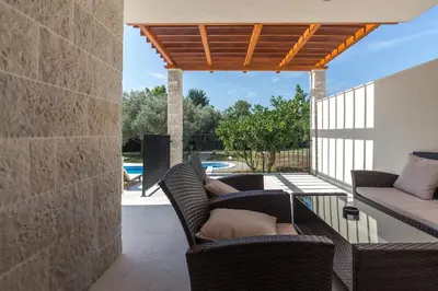 a patio with wicker chairs and a wooden pergola at Villa Zen Port in Petrovac na Moru