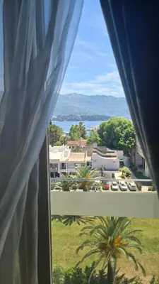a window with a view of a house and a palm tree at Apartments M Palace in Budva
