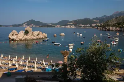 a beach with umbrellas and boats in the water at Mima Apartments in Sveti Stefan