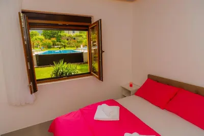 a bedroom with a red bed and a window and a pool at Apartmani Novaković in Kotor