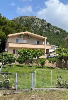 a house with a fence in front of a mountain at Apartmani Joca in Sutomore