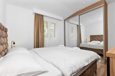 a white bedroom with two beds and a mirror at Apartments Dončić in Kotor