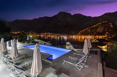 a pool with chairs and umbrellas at night at Apartments Dončić in Kotor