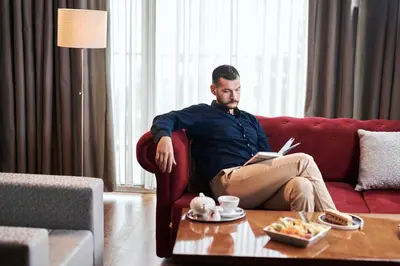 a man sitting on a couch reading a book at Ramada by Wyndham Podgorica in Podgorica