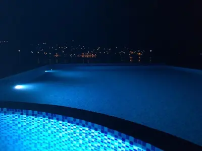 a swimming pool at night with a city in the background at Apartments Komina in Utjeha