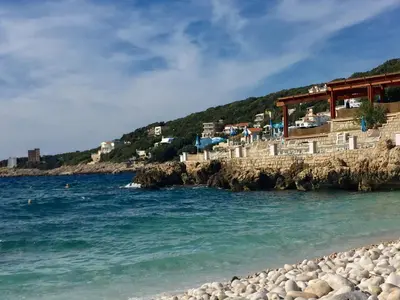 a beach next to the ocean with buildings on a cliff at Apartmani Milanovic Susanj in Bar