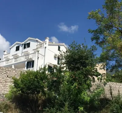 a white house on top of a stone wall at Apartmani Dragović in Sveti Stefan