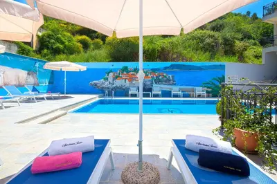 a pool with two blue benches and an umbrella at Apartments Jovan in Sveti Stefan