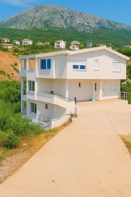 a white apartment building with a mountain in the background at Apartments Lejla in Dobra Voda