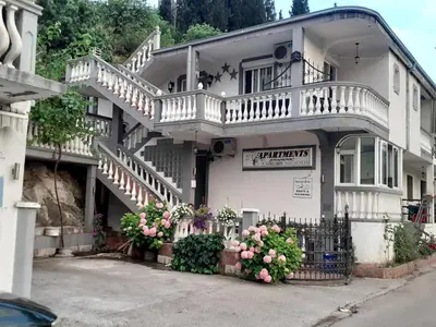 a white building with a balcony and flowers at Apartments FLORA and boat cruising in Virpazar