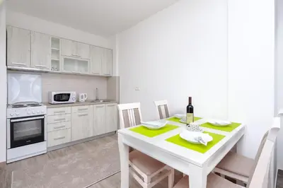 a white kitchen with a white table and chairs at Apartment Sidro in Petrovac na Moru