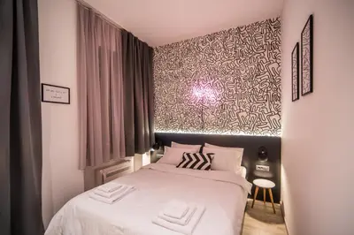 a bedroom with a bed with white sheets and pink pillows at Hotel Marienplatz Podgorica in Podgorica