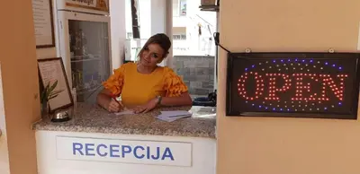 a woman standing at a counter next to a sign at Apartments Cindrak in Bar