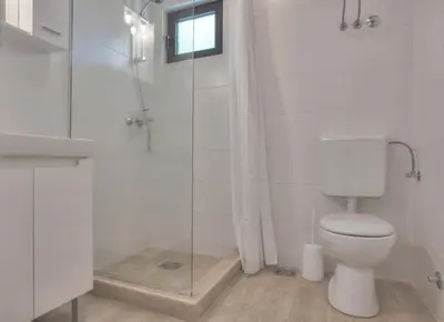 a white bathroom with a toilet and a glass shower at Gregovic Family Apartments in Petrovac na Moru