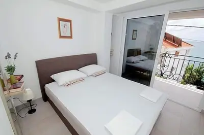 a white bedroom with a large bed and a balcony at Apartmani Kasija in Dobra Voda