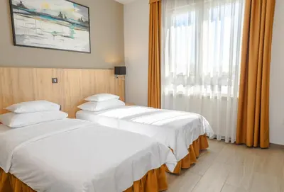 two beds in a hotel room with a window at Hotel Resurs in Podgorica
