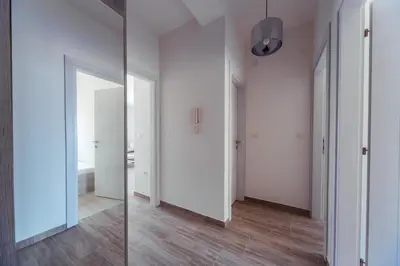 a hallway with white walls and wood floors and a mirror at Belvedere Apartments in Petrovac na Moru