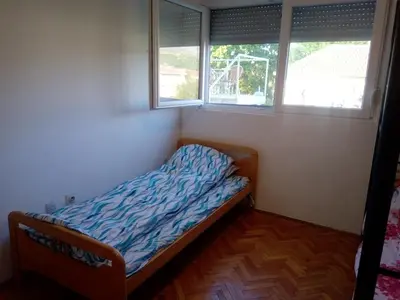 a small bed in a room with two windows at Hostel Olea in Podgorica