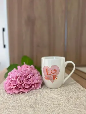 a cup with a heart painted on it next to a pink flower at Apartments Hillside in Ulcinj