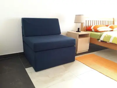a blue chair in a bedroom with a bed at Pensions Airport in Podgorica