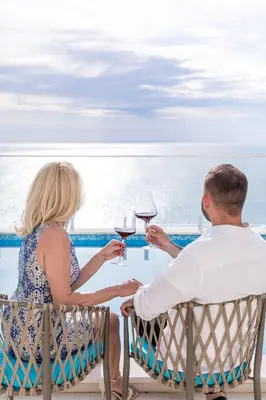 a man and woman sitting at a table with glasses of wine at ĀNANTI Resort, Residences & Beach Club - The Leading Hotels of the World in Sveti Stefan