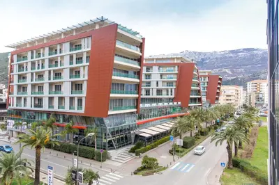 a tall red building with a street and palm trees at Central Budva apartment in Budva
