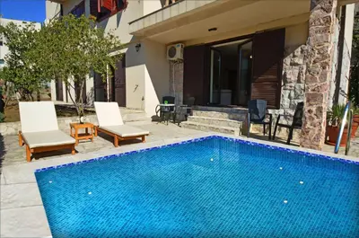 a blue swimming pool with two chairs and a house at DC Apartment C in Kotor