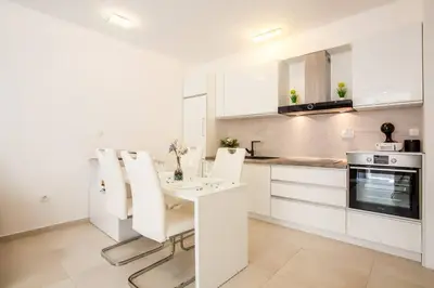 a white kitchen with a table and white chairs at Lux Apartment Teodora Rafailovici in Rafailovici
