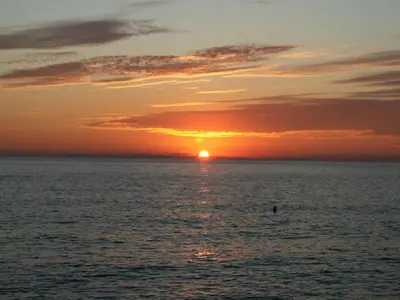 a sunset over the ocean with a person in the water at Apartments Galija in Petrovac na Moru