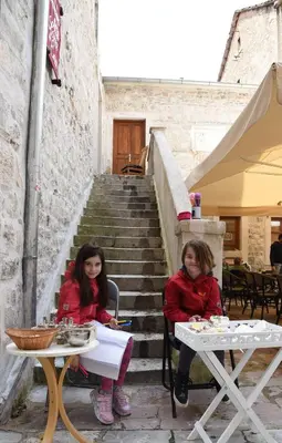 two girls sitting at tables in front of some stairs at Lana & Ena Apartments in Kotor