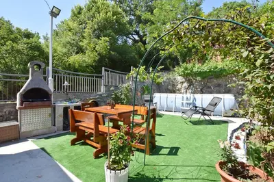 a patio with a table and a grill and grass at Apartments Siljak in Petrovac na Moru