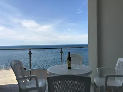 a table with a bottle of wine on a balcony with the ocean at First line of the sea 1 in Dobra Voda
