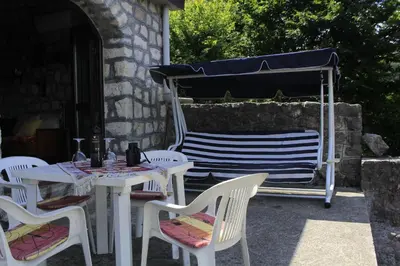 a patio with white tables and chairs and a grill at Rent House Orahovo in Virpazar