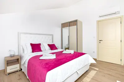 a white bedroom with a large bed with a red blanket at Apartments Mezini 11 in Kotor