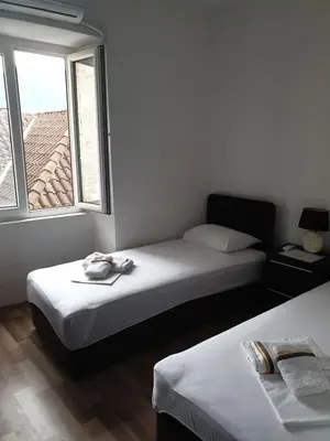 two beds in a room with a window at Nova dvokrevetna soba sa dva odvojena kreveta i zajedničkim kupatilom in Kotor