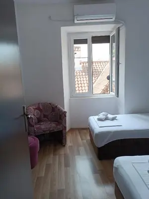 a room with two beds and a chair and a window at Nova dvokrevetna soba sa dva odvojena kreveta i zajedničkim kupatilom in Kotor