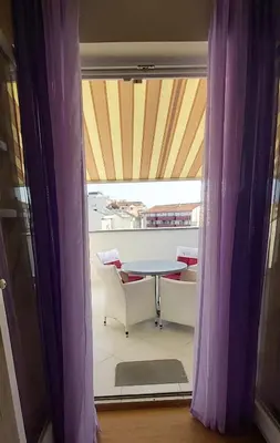a table and chairs on a balcony with purple curtains at Sunčani apartman 1-Vila Amfora in Budva