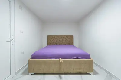 a bed with purple sheets in a white room at Stojkovic Family Apartments in Tivat