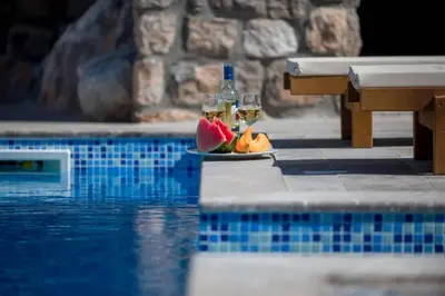 a plate of fruit and wine glasses next to a swimming pool at Villa Old Castle Apartments in Kotor