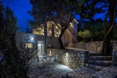 a house with a stone wall and a table and chairs at Dolores Apartments in Petrovac na Moru