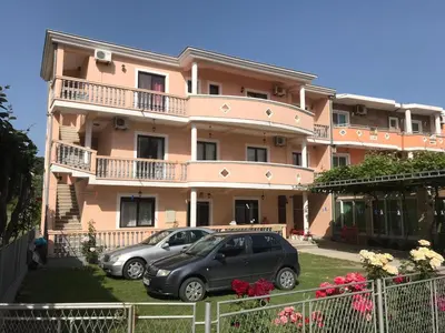 two cars parked in front of a pink building at Rooms Ibrocevic in Ulcinj