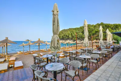 a row of tables and chairs with umbrellas on a beach at Hotel Plaza Lucice in Petrovac na Moru