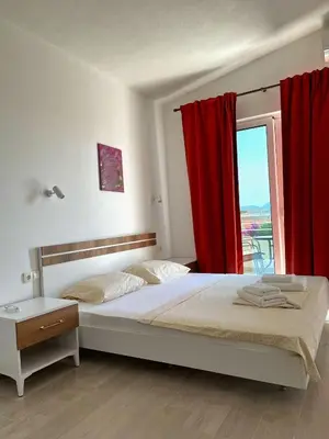 a bedroom with a bed and a window with red curtains at Apartmani Vila Milaris in Ulcinj