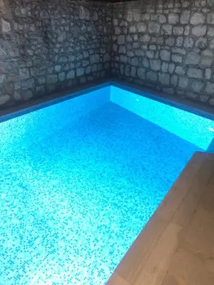 a swimming pool with blue water in front of a stone wall at Luxury Waterfront Villa with Private Pool and Private Beach for 12 People in Kotor