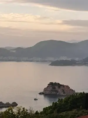 a boat in a large body of water with mountains at Apartments Dragišić in Sveti Stefan