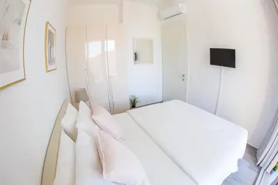a white bedroom with a bed with white sheets and pillows at Apart SKY Residence with sea view in DELMAR in Budva