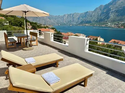 a balcony with chairs and an umbrella and a view of the water at House with big terrace and beautiful sea view in Kotor